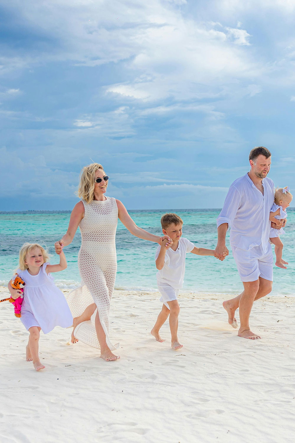 family of five with young kids walking happily on a white sandy beach in the Maldives