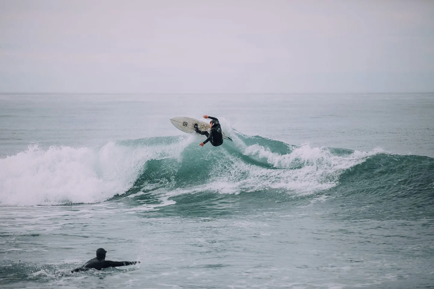 Two men are practicing surfing on a cold cloudy day