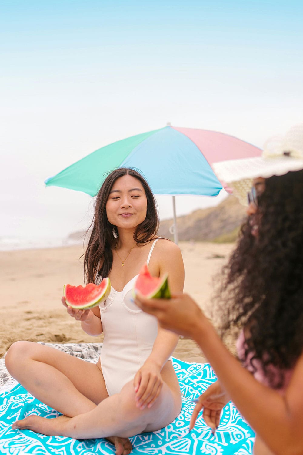 two woman friends eating watermelon at the beach