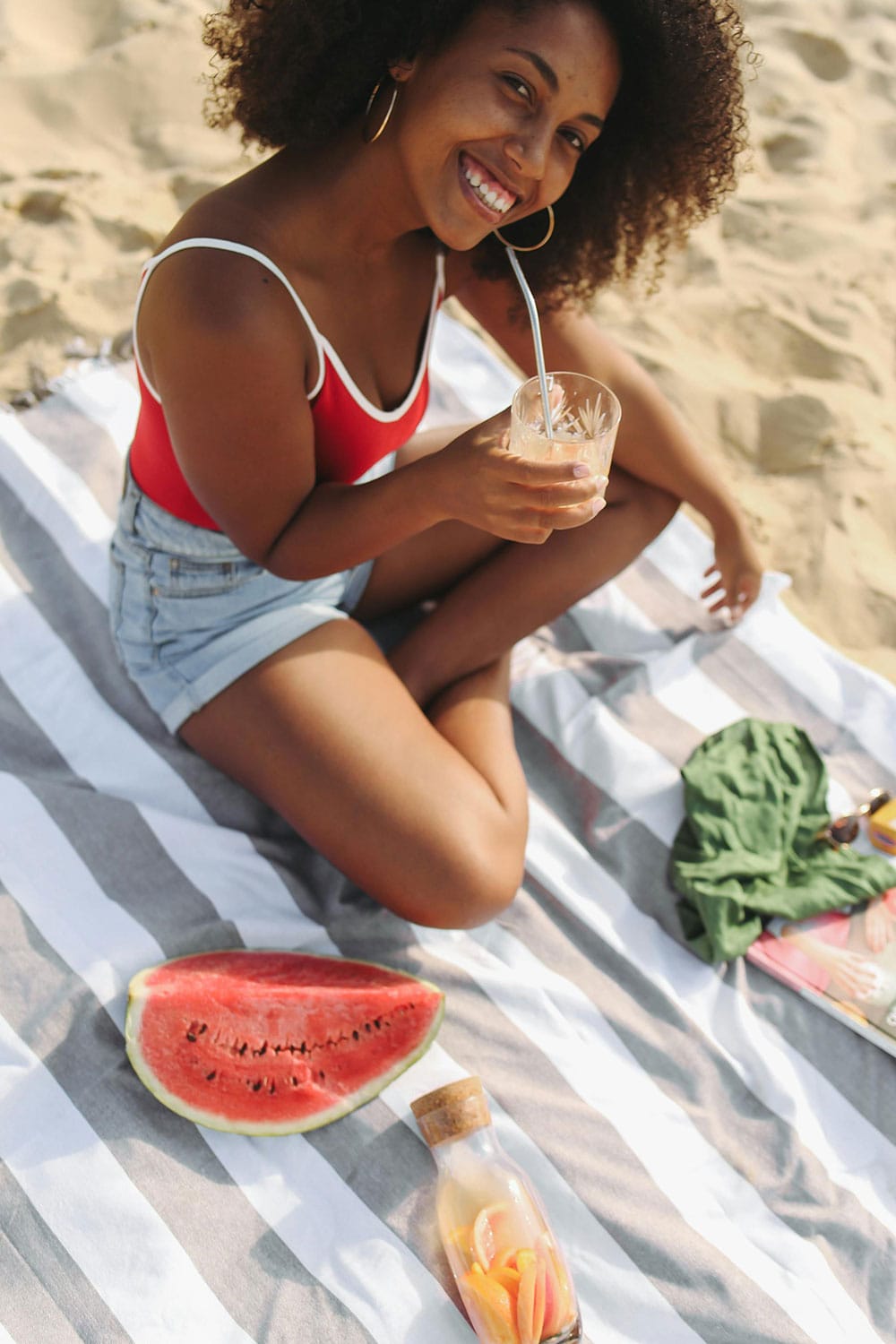woman sitting on beach towel with cold lemonade in hand