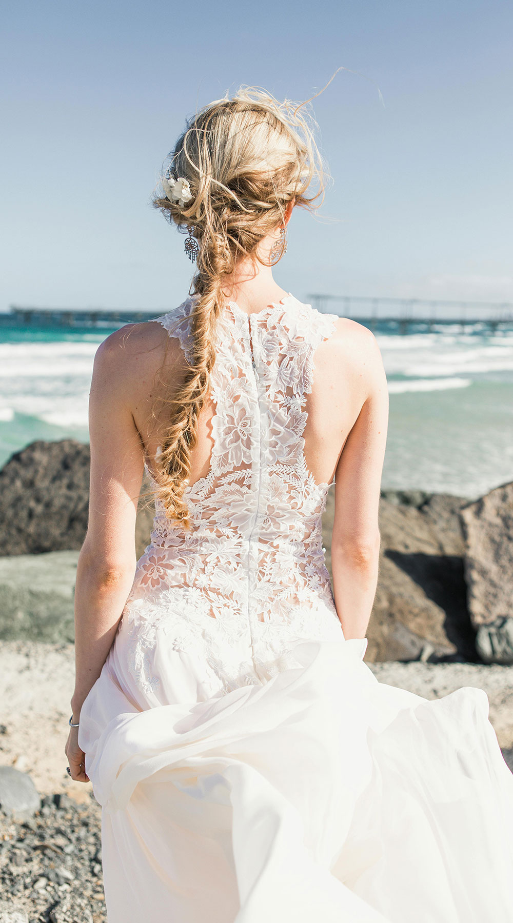 woman in white lace wedding dress and with fishtail braid hair standing near the ocean