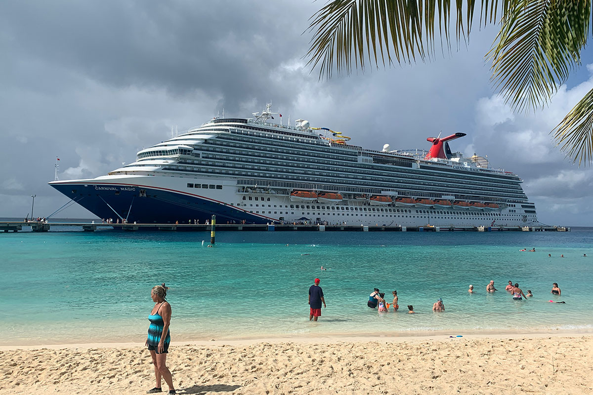Carnival Magic cruise ship docked at a Caribbean destination, while people enjoying the beach