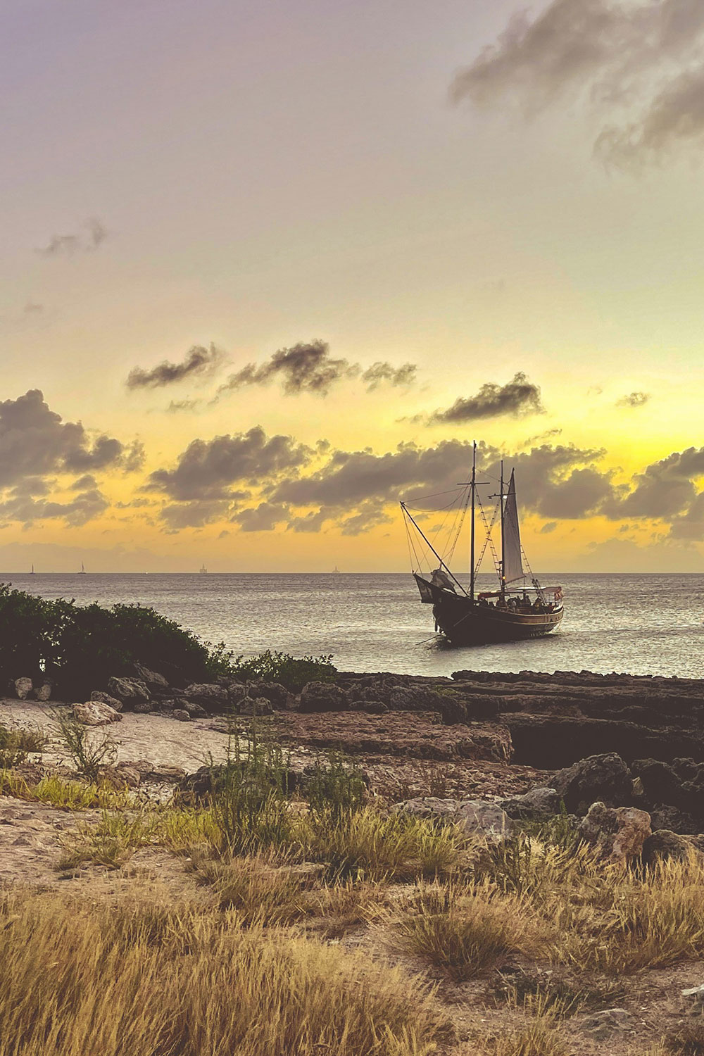 wooden boat is sailing close to the shore during sunset in Aruba