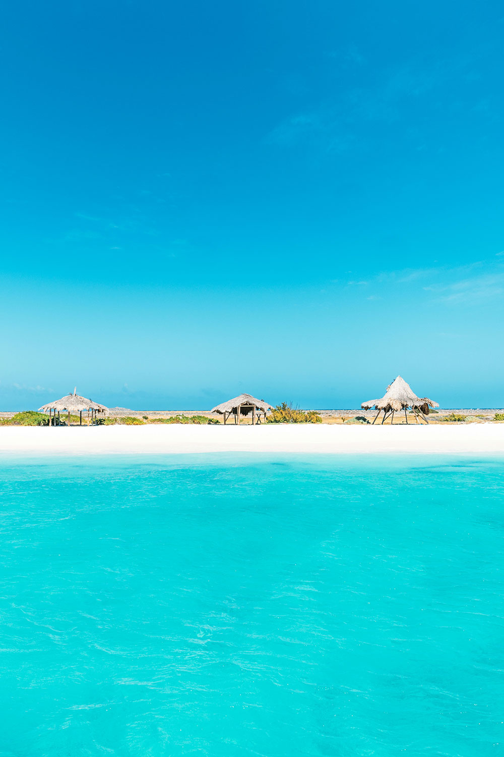 white sand beach with some huts on it on the uninhabited Caribbean island of Klein Curaçao