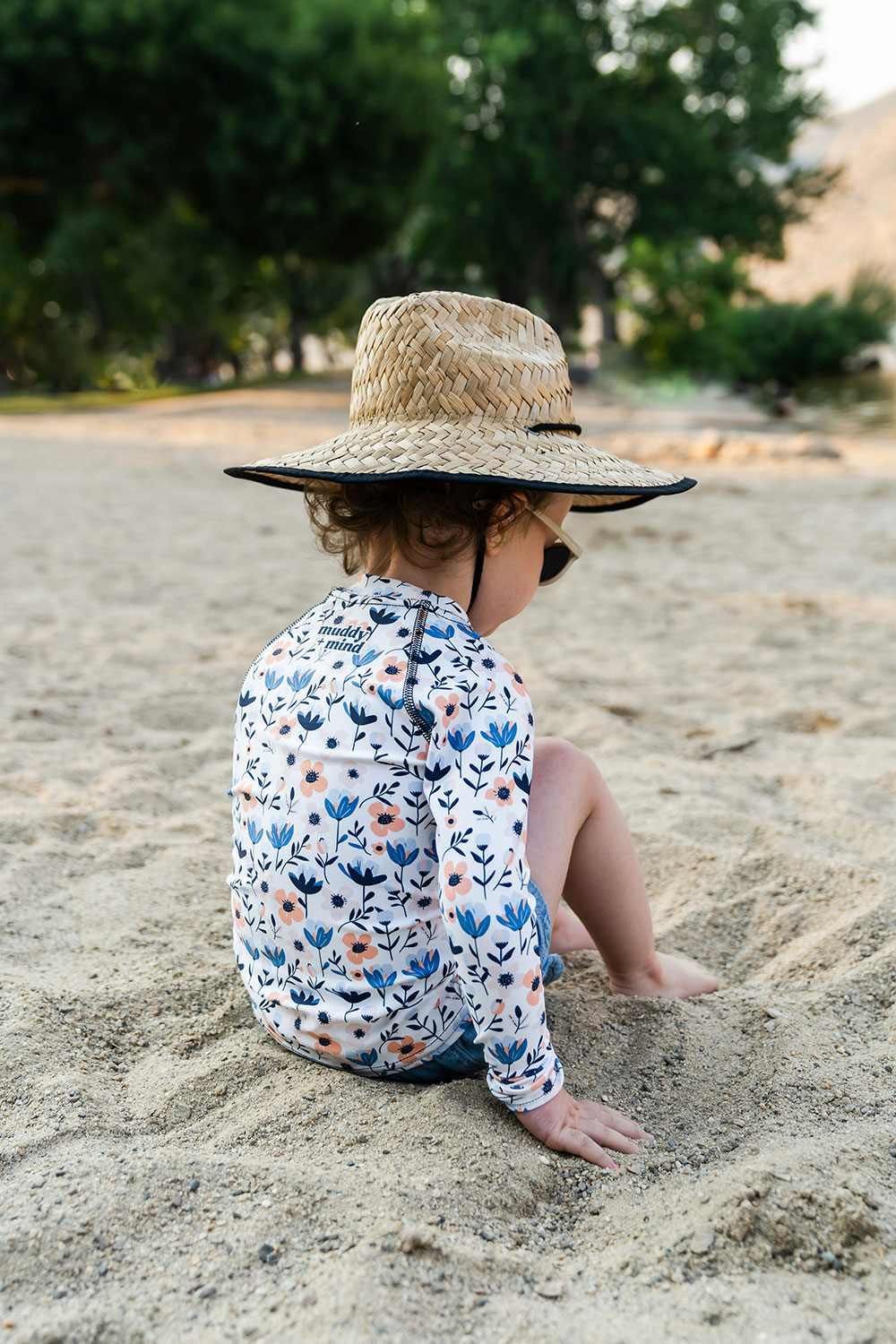 child wearing a floral print rashguard and a straw hat on the beach
